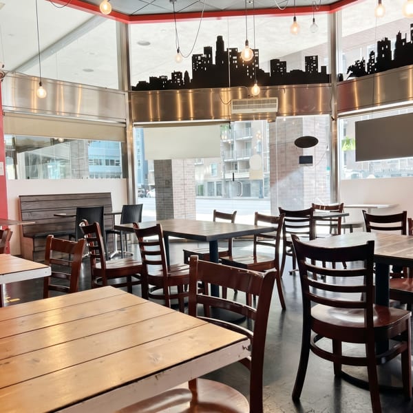 A restaurant dining room with wooden tables and chairs, city skyline decor, and large windows.