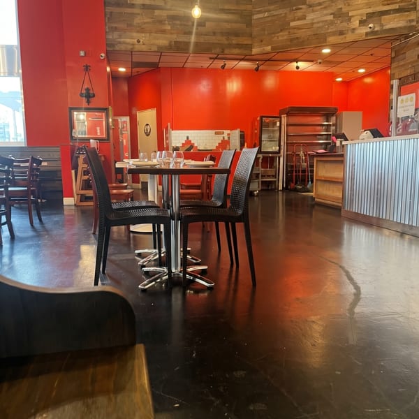 Empty restaurant interior with red walls, wooden accents, black chairs, and set tables.