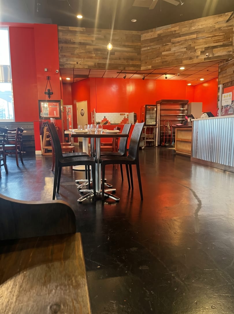 Empty restaurant interior with red walls, wooden accents, black chairs, and set tables.